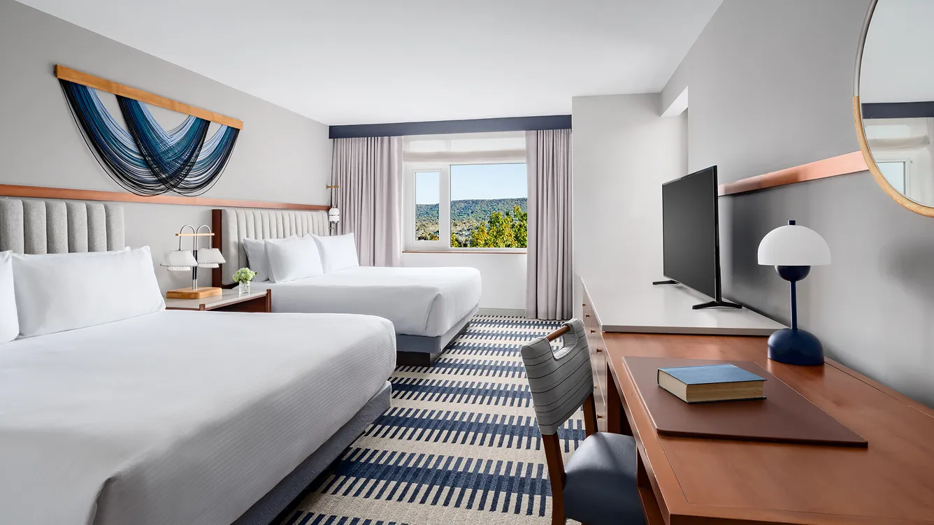 Modern hotel room with two beds and desk.