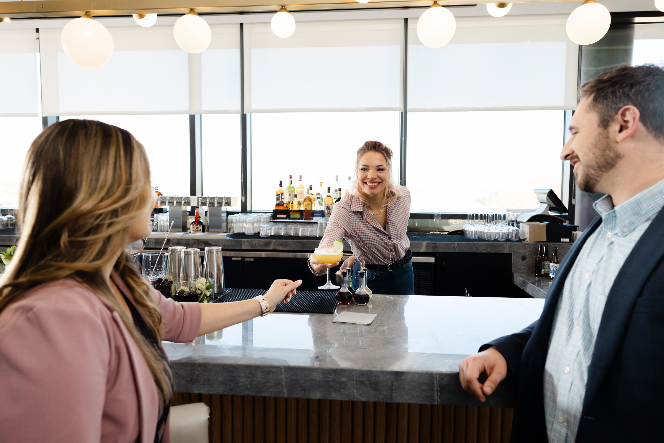 Bartender serving drinks to two customers.